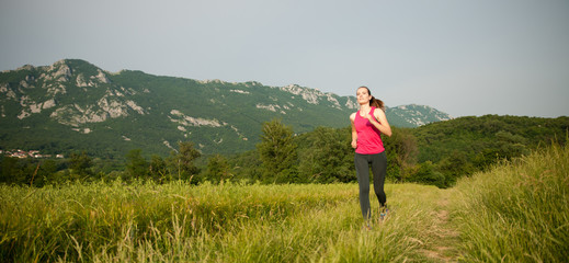 Beautiful young woman workout outdoor runs across meadow in early summer