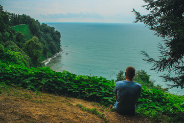 Fototapeta premium Silhouette of a young guy who sits on the edge of the observation deck in the botanical garden of Batumi