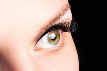 Female green eye with long eyelashes on the black background close-up. Eyelash extensions, lamination, cosmetology, ophthalmology concept. Good vision, clear skin.