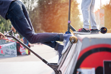 Teenagers wearing sneakers riding scooters on ramp  in skate park