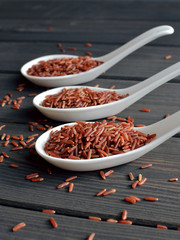 Red rice in ceramic spoons on dark wooden background