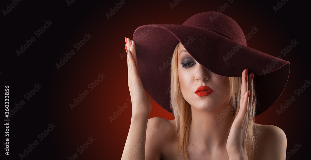 Wall mural beautiful blond woman with pure skin. evening make-up on the red background in a red hat.