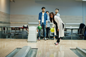 South asian woman standing at bowling alley with ball on hands. Girl is preparing for a throw.