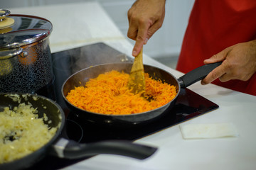 man chef cooks carrots and onions on an electric stove in a black frying pan