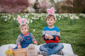 Little cute boy and girl are sitting on the grass near the daffodils. Children in costumes Easter bunnies.