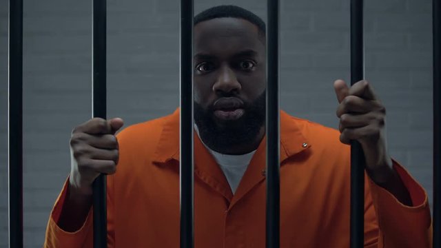 Anxious afro-american prisoner holding bars and threatening to camera, criminal
