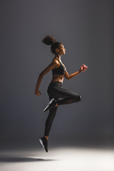 side view of beautiful athletic african american sportswoman jumping on black