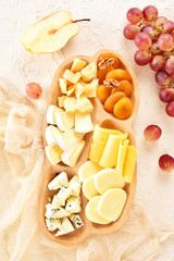 Cheese set on a plate laid out on a beige background. Different types of cheeses: Camembert, Parmesan, blue cheese, olives, honey, grapes.