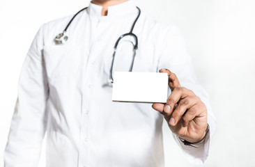 Handsome young doctor in a white coat with a stethoscope holds on the outstretched hand a blank white package box for blister of pills. Mock up.