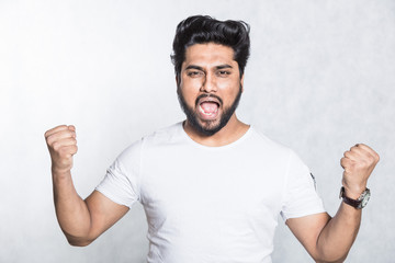 Fototapeta premium Portrait of overjoyed man clenches fists with happiness, poses against white background.