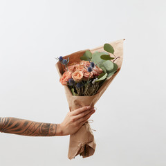 Delicate flowers living coral roses and eryngium as a beautiful bouquet in girl's hand with tattoo,...