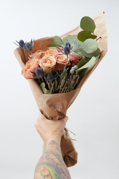 Woman's hand with tattoo is holding beautiful colored living coral rores bouquet. Greeting card for Mother's or Woman's Day. Copy space.
