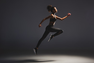 Fototapeta na wymiar side view of beautiful athletic african american sportswoman jumping on black