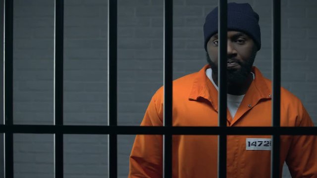 Aggressive afro-american prisoner in camera holding cell bars, life sentence