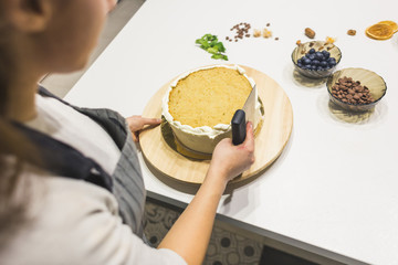 Confectioner smooths white cream on a biscuit cake with a cooking spatula. The concept of homemade pastry, cooking cakes.