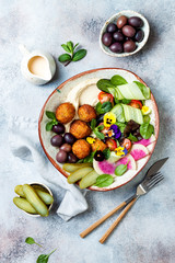 Middle eastern lunch Buddha bowl with hummus, falafel, tomato and greens salad, olives, pickles and edible flowers