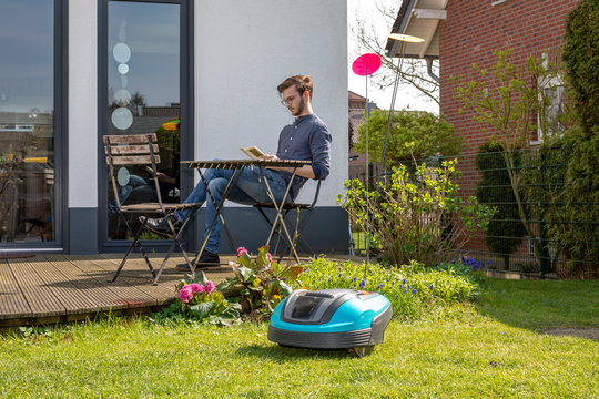 Roboterrasenm&auml;her im Hintergrund Mann mit Buch