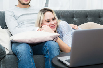 Young beautiful couple resting on the couch and watching online video from a laptop in the living room.