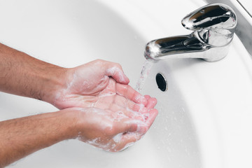 Adult caucasian male washing hands with soap under the faucet with water