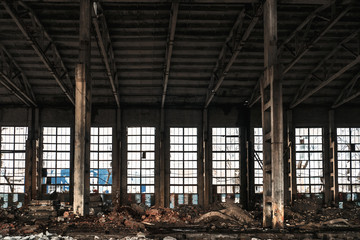 Warehouse with big windows, columns and debris of abandoned and ruined industrial factory building interior