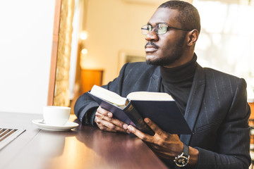 Young handsome dark-skinned businessman in a cafe reads a book with a cup of tea.