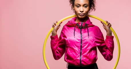 panoramic shot of beautiful african american sportswoman with hula hoop looking at camera isolated on pink