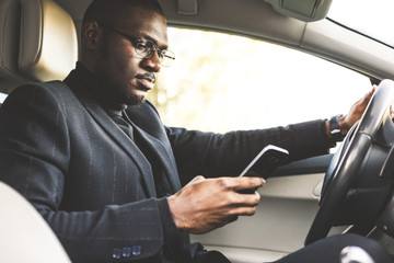 A businessman driving a expensive car holds a mobile phone in his hand. Hasty life.