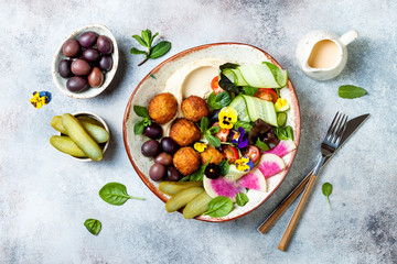 Middle eastern lunch Buddha bowl with hummus, falafel, tomato and greens salad, olives, pickles and edible flowers