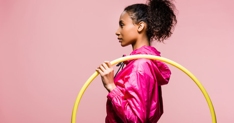 panoramic shot of beautiful african american sportswoman posing with hula hoop isolated on pink...