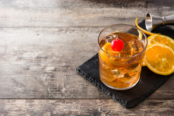 Old fashioned cocktail with orange and cherry on wooden table. Copyspace