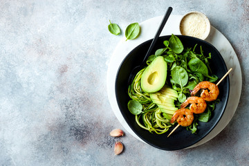 Detox Buddha bowl with avocado, spinach, greens, zucchini noodles, grilled shrimps and pesto sauce. Vegetarian vegetable low carb lunch bowl.