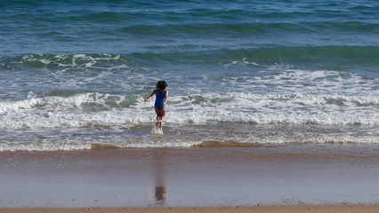 Rear view of a young girl in blue swimsuit. It bathes with much fun in the sea and jumps over the waves.