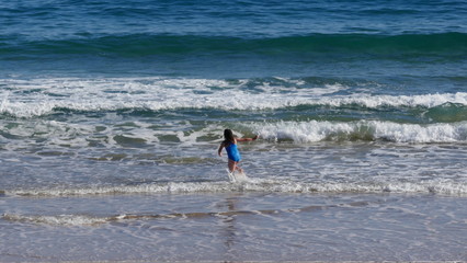Rear view of a young girl in blue swimsuit. It bathes with much fun in the sea and jumps over the waves.