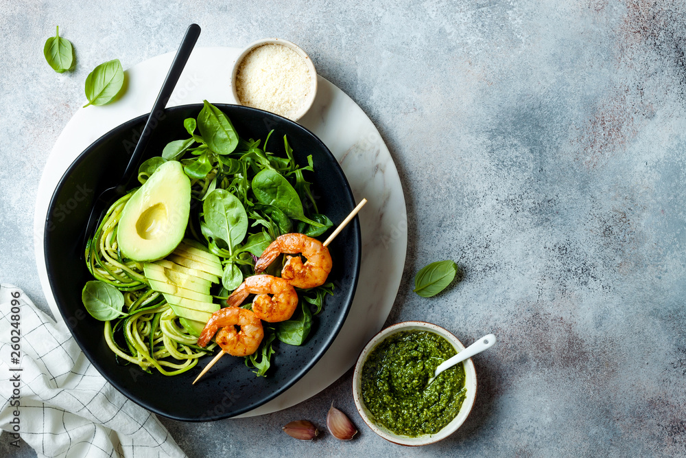 Wall mural Detox Buddha bowl with avocado, spinach, greens, zucchini noodles, grilled shrimps and pesto sauce. Vegetarian vegetable low carb lunch bowl.