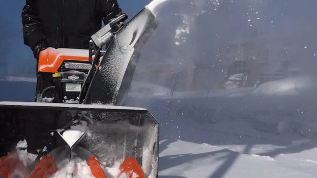 A man cleans the snow with a snowblower during a snowfall. Slow motion.