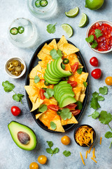 Yellow corn nachos chips with melted cheese sauce, avocado, jalapeno, cilantro leaves, tomato salsa and spicy iced margarita cocktail