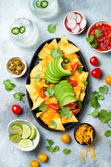 Yellow corn nachos chips with melted cheese sauce, avocado, jalapeno, cilantro leaves, tomato salsa and spicy iced margarita cocktail