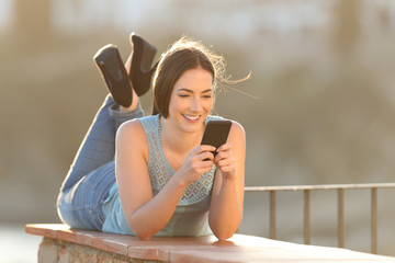 Happy woman using a smart phone lying in a balcony