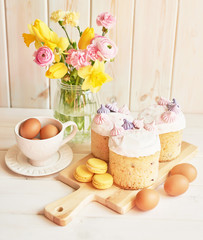 Easter cakes on the table, macaroons, eggs and a bouquet of flowers in a vase near on a white background