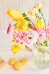Fototapeta na wymiar bouquet of spring flowers: tulips, carnations, ranunculi and daffodils in a vase on a table on a white wooden background