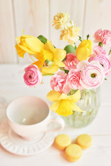 cup near with a vase with a bouquet of spring flowers on a wooden background