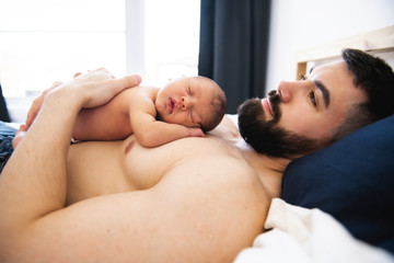 father lay on bed with his newborn baby daughter