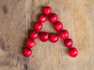 cherries on wooden background as a letter
