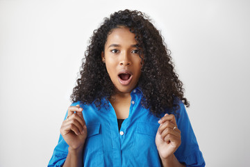 Fototapeta na wymiar I can't believe it. Casually dressed young Afro American woman employee with curly hairdo keeping mouth wide opened, demonstrating true reaction, surprised with unexpected promotion at work