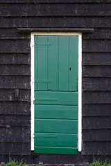 Front door of small rural cottage house with wooden wall and green door