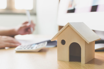 Wooden home model and key house on wood table with hand signing the document contract loan or...