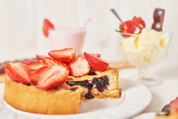 Strawberry cake and chocolate bars on a white wooden background.