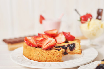 Strawberry cake and chocolate bars on a white wooden background.