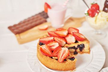 Strawberry cake and chocolate bars on a white wooden background.