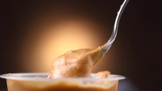 Peanut butter. Creamy smooth peanut butter in jar on a table. Spoon on Natural nutrition, organic food. American cuisine. 4K UHD video, slow motion